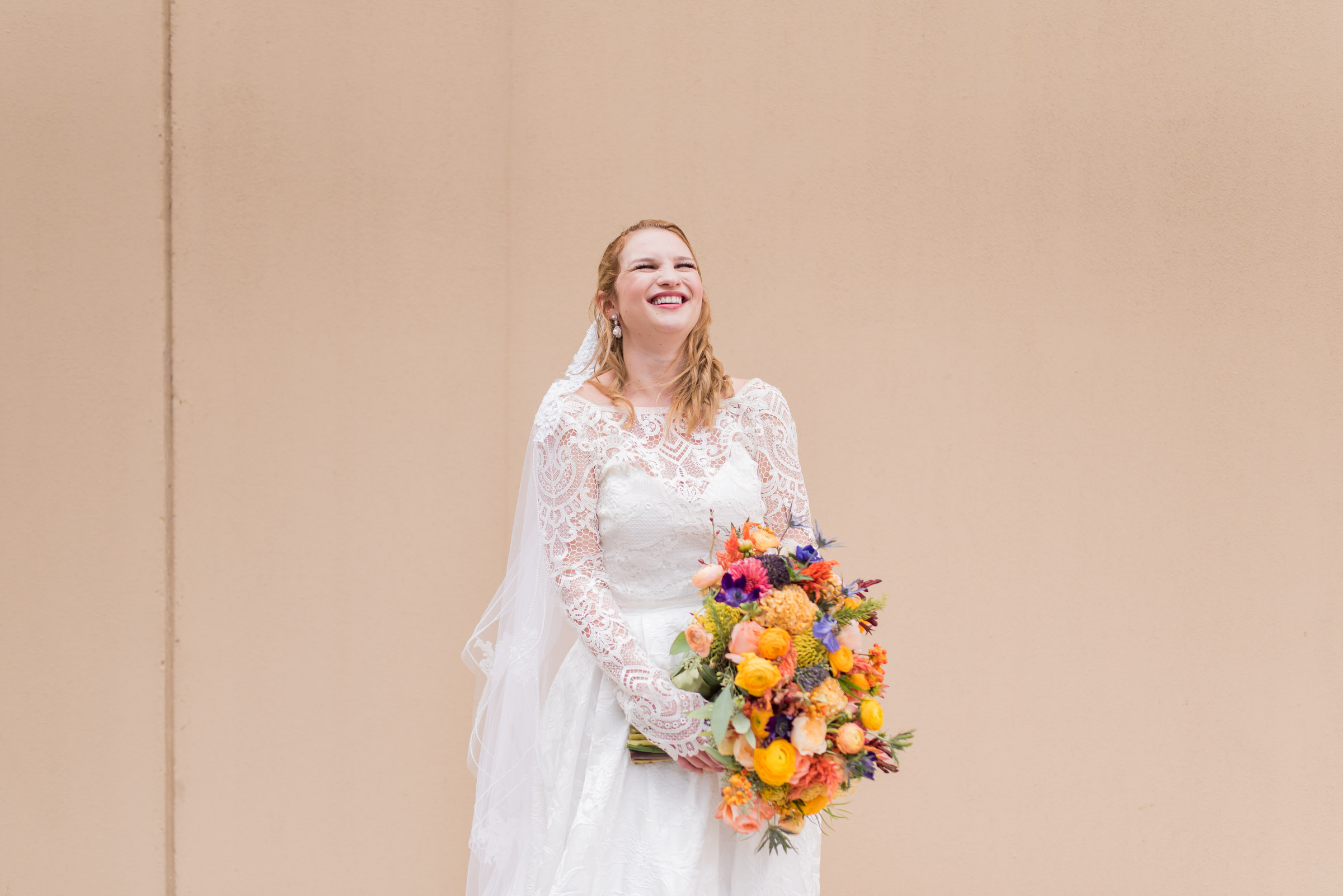 columbus, ga wedding at the powerhouses, laughing fall bride in front of blank wall with colorful fall flowers