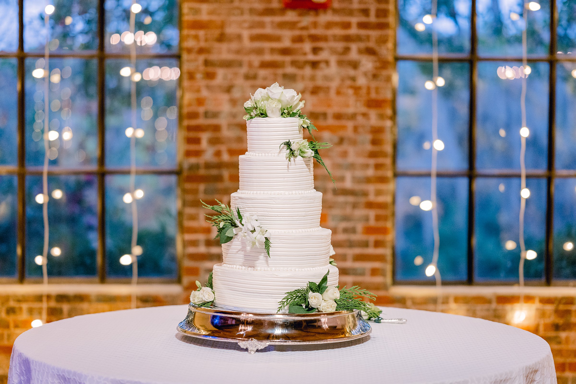 Columbus, Ga wedding at the Bibb Mill - white tiered wedding cake with green and white flowers sitting atop a silver tray